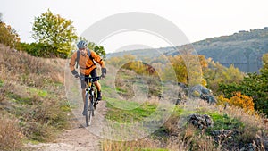 Cyclist in Orange Riding the Mountain Bike on the Autumn Rocky Trail. Extreme Sport and Enduro Biking Concept.