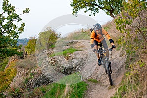 Cyclist in Orange Riding the Mountain Bike on the Autumn Rocky Trail. Extreme Sport and Enduro Biking Concept.