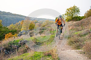 Cyclist in Orange Riding the Mountain Bike on the Autumn Rocky Trail. Extreme Sport and Enduro Biking Concept.