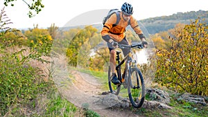 Cyclist in Orange Riding the Mountain Bike on the Autumn Rocky Trail. Extreme Sport and Enduro Biking Concept. photo