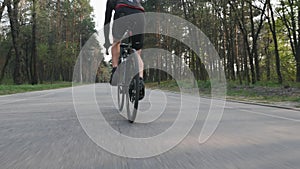 Cyclist pedaling on bicycle close up leg muscle view. Bike rider in the park wearing black sportswear.