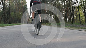 Cyclist pedaling on bicycle close up leg muscle view. Bike rider in the park wearing black sportswear. Slow motion