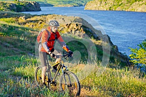 Cyclist in Red Jacket Riding Mountain Bike on the Beautiful Spring Trail above Blue River. Travel and Adventure Sport Concept