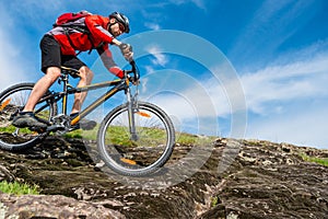 Cyclist in Red Jacket Riding Mountain Bike Down Rocky Hill. Extreme Sport and Adventure Concept.