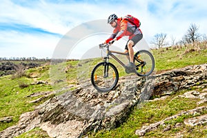 Cyclist in Red Jacket Riding Mountain Bike Down Rocky Hill. Extreme Sport and Adventure Concept.