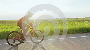 Cyclist in red outfit training on road bicycle at sunset