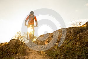 Cyclist in Red Riding the Bike on Autumn Rocky Trail at Sunset. Extreme Sport and Enduro Biking Concept.