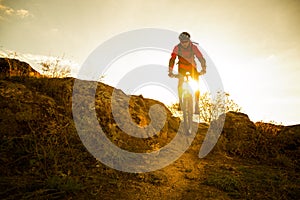 Cyclist in Red Riding the Bike on Autumn Rocky Trail at Sunset. Extreme Sport and Enduro Biking Concept.