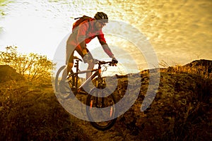 Cyclist in Red Riding the Bike on Autumn Rocky Trail at Sunset. Extreme Sport and Enduro Biking Concept.