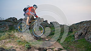 Cyclist in Red Riding the Bike on Autumn Rocky Trail at Sunset. Extreme Sport and Enduro Biking Concept.