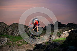 Cyclist in Red Riding the Bike on Autumn Rocky Trail at Sunset. Extreme Sport and Enduro Biking Concept.