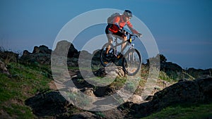 Cyclist in Red Riding the Bike on Autumn Rocky Trail at Sunset. Extreme Sport and Enduro Biking Concept.