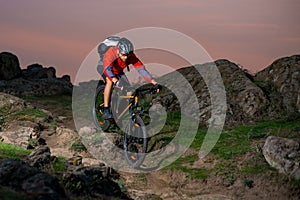 Cyclist in Red Riding the Bike on Autumn Rocky Trail at Sunset. Extreme Sport and Enduro Biking Concept.