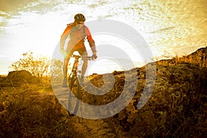 Cyclist in Red Riding the Bike on Autumn Rocky Trail at Sunset. Extreme Sport and Enduro Biking Concept.