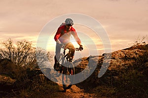 Cyclist in Red Riding Bike on the Autumn Rocky Trail at Sunset. Extreme Sport and Enduro Biking Concept.