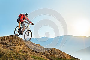 Cyclist in Red Riding the Bike Down the Rock at Sunrise. Extreme Sport and Enduro Biking Concept. photo