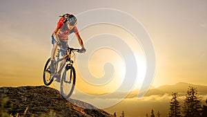 Cyclist in Red Riding the Bike Down the Rock at Sunrise. Extreme Sport and Enduro Biking Concept.