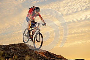 Cyclist in Red Riding the Bike Down the Rock at Sunset. Extreme Sport and Enduro Biking Concept.