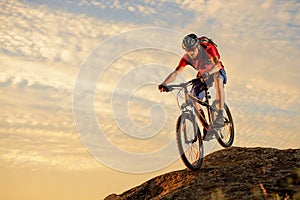 Cyclist in Red Riding the Bike Down the Rock at Sunset. Extreme Sport and Enduro Biking Concept.