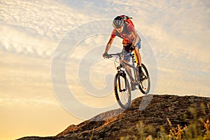 Cyclist in Red Riding the Bike Down the Rock at Sunset. Extreme Sport and Enduro Biking Concept.