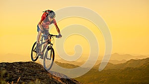 Cyclist in Red Riding the Bike Down the Rock at Sunset. Extreme Sport and Enduro Biking Concept.