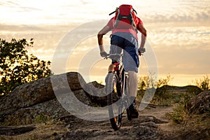 Cyclist in Red Riding the Bike on the Rocky Trail at Sunset. Extreme Sport and Enduro Biking Concept.
