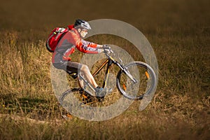 Cyclist in Red Riding the Mountain Bike on the Trail in Field. Extreme Sport Concept. Manual or Weelie on MTB.