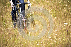 Cyclist rides through the field with wild flowers and grass