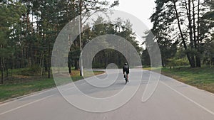 Cyclist riding alone in the park while training for race. Back follow shot of cyclist pedaling road bicycle. Slow motion