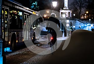 Cyclist riding alongside the bus in the illuminated city at night