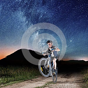 Cyclist riding bike in the night under starry sky