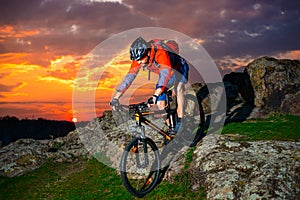 Cyclist Riding Mountain Bike Down Spring Rocky Hill at Beautiful Sunset. Extreme Sports and Adventure Concept. photo