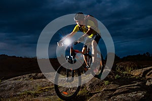 Cyclist Riding the Mountain Bike on Rocky Trail at Night. Extreme Sport and Enduro Biking Concept.