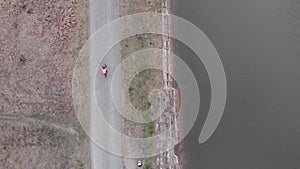 Cyclist riding near dam, drone top view. Woman in bike apparel cycling outdoor on gravel bike. Professional triathlete hard pedall