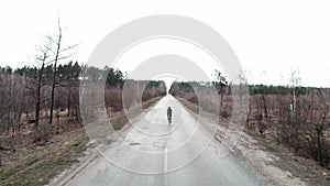 Cyclist riding outdoor. Person in black cycling apparel rides road bike on empty car road in forest. Cyclist pedaling on bike. End