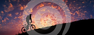 Cyclist riding uphill against majestic colorful sunset