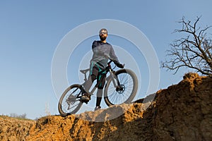 Cyclist in shorts and jersey on a modern carbon hardtail bike with an air suspension fork standing on a cliff against the backgrou