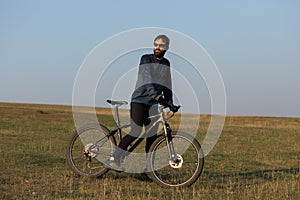 Cyclist in shorts and jersey on a modern carbon hardtail bike with an air suspension fork standing on a cliff against the backgrou