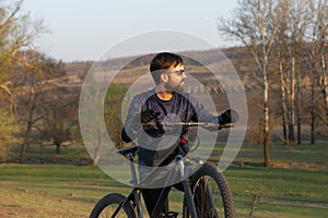 Cyclist in shorts and jersey on a modern carbon hardtail bike with an air suspension fork standing on a cliff against the backgrou