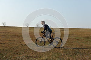 Cyclist in shorts and jersey on a modern carbon hardtail bike with an air suspension fork standing on a cliff against the backgrou photo