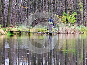 Cyclist stay at his trekking bike on small pond pier and watching swans