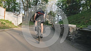 Cyclist with strong legs pedaling out of the saddle climbing the hill. Cycling training concept. Follow shot. Slow motion