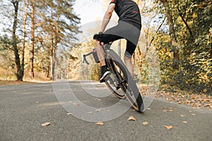 Cyclist tricks on bicycle on road in autumn forest, photo behind, focus on wheel. Man rides a bicycle ride on a country road in