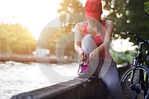 Cyclist woman sitting and tying shoeslace along the canal in sunset