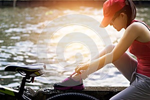 Cyclist woman sitting and tying shoeslace along the canal in sunset