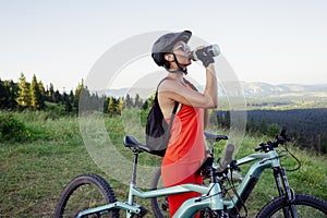 Cyclist woman standing with bike and drinking water