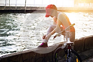 Cyclist woman tying shoeslace along the canal in sunset