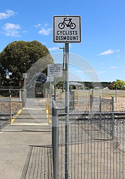 Cyclists dismount sign at a railway crossing with a blue sky