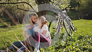 Cyclists man and woman sat under a tree on the background of his bike.