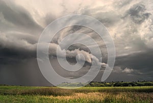 Cyclone storm over fields and meadows approaches the hilly valley. Rainy cloudy day